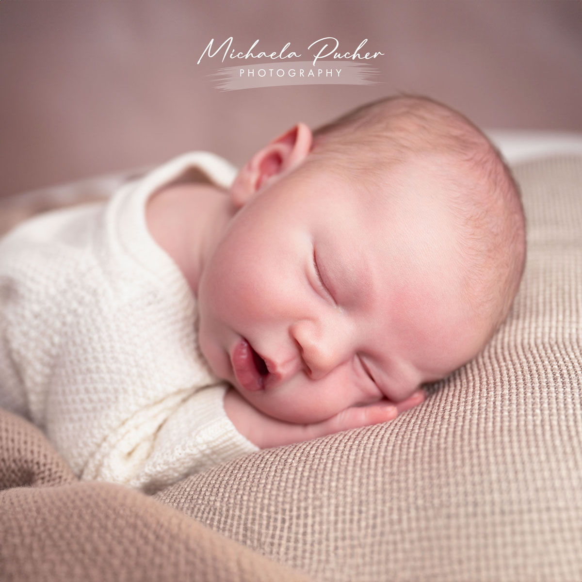 Schlafendes Neugeborenes mit leicht geöffnetem Mund, gebettet auf weichen Stoffen in warmen Naturtönen.